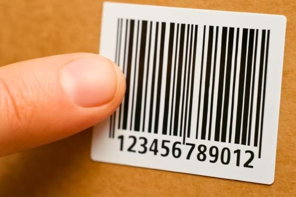 un doigt humain pointant une &eacute;tiquette de code-barres sur une texture de carton brun.