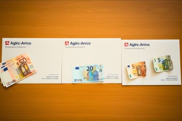 trois enveloppes de pension Agirc-Arrco align&eacute;es sur une table, avec des billets 