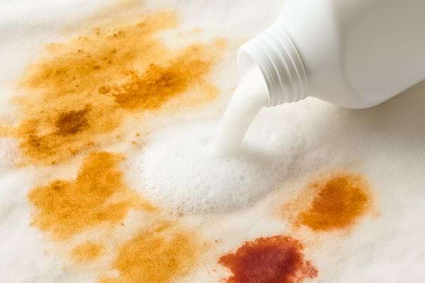 Du detergent liquide est verse sur des taches orange sur un tissu blanc.