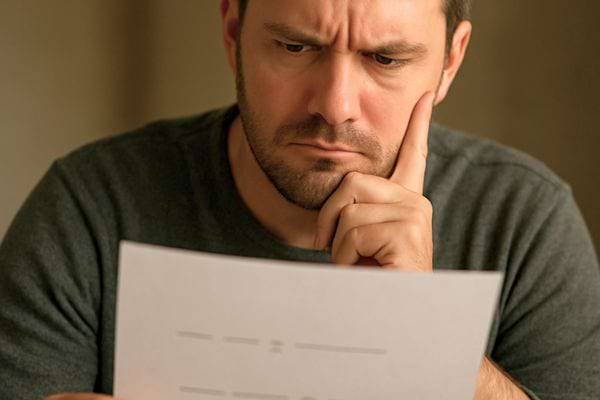 homme barbu regarde un document avec concentration la main sur le visage dans une atmosphere studieuse