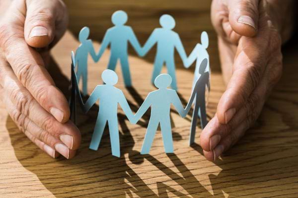 Des mains entourent un cercle de figurines en papier symbolisant la protection familiale.