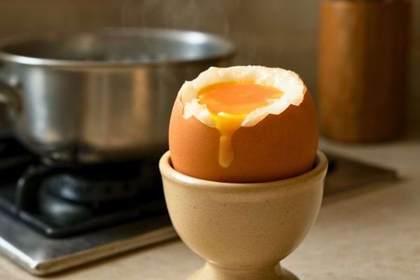 oeuf a la coque ouvert avec jaune liquide dans un coquetier pres dune casserole chaude