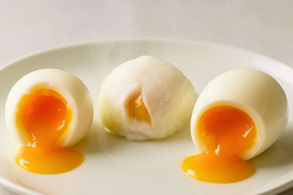trois oeufs mollets ouverts avec jaune coulant presentes sur une assiette blanche