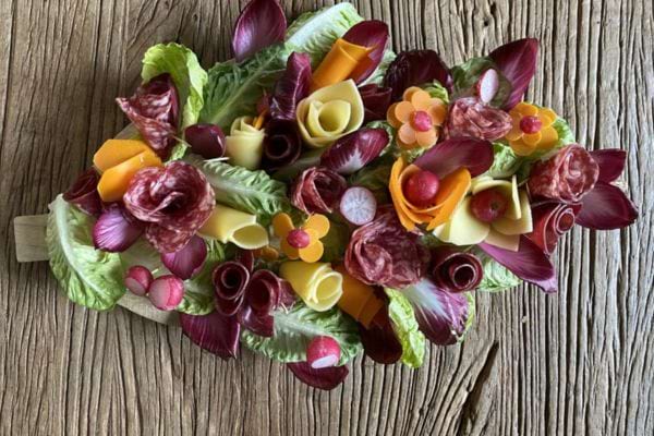 un plateau ap&eacute;ritif avec de la charcuterie, des l&eacute;gumes et du fromage en forme de bouquet.