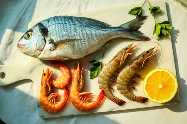 poisson entier cru avec crevettes citron et herbes presentes sur une planche de cuisine