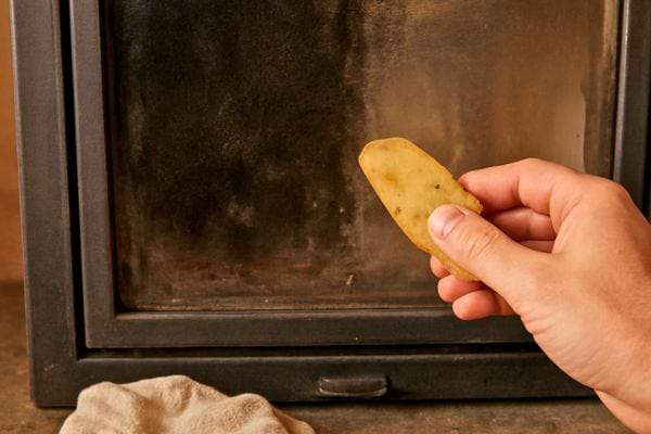 main frottant une pomme de terre sur la vitre dun poele pour enlever suie et traces