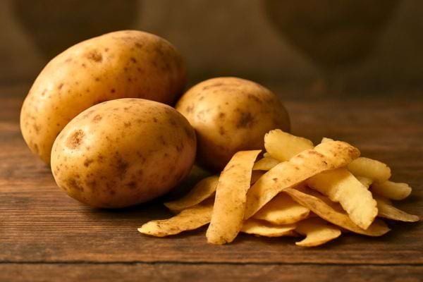 Pommes de terre entieres et epluchures posees sur table en bois