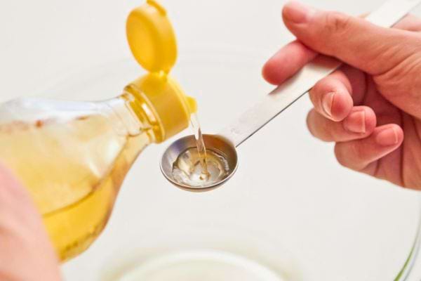 main versant du vinaigre dans une cuillere doseuse au dessus dun recipient transparent