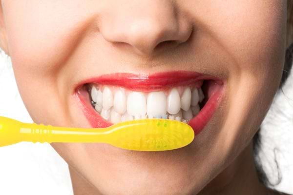 gros plan sur un sourire avec une brosse a dents jaune