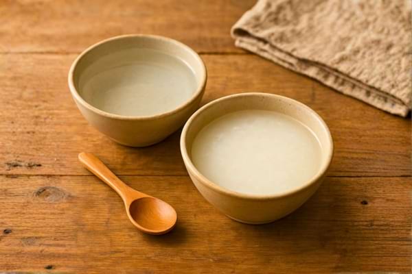deux bols sur un plan de travail en bois. L'un contient de l'eau claire, l'autre de l'eau de riz laiteuse.
