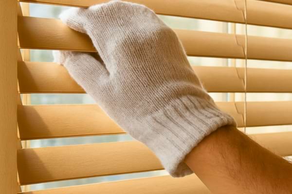 Une main portant une chaussette en coton blanc pour nettoyer un store