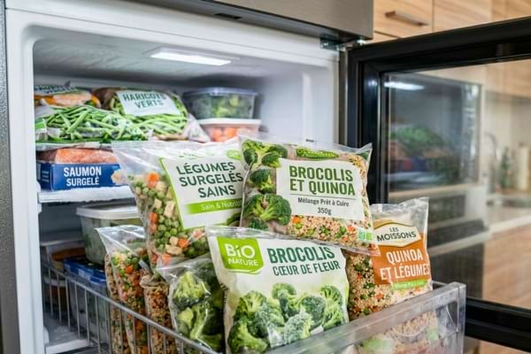 un cong&eacute;lateur moderne ouvert, rempli de sachets de l&eacute;gumes surgel&eacute;s sains, brocolis et quinoa