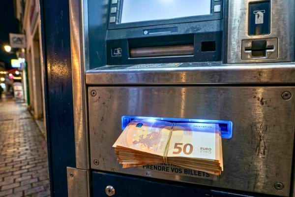 ne &eacute;paisse liasse de billets en euros sortant de la fente d'un distributeur automatique