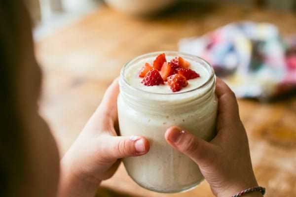 des mains d'enfant tenant fièrement un pot de yaourt en verre fait maison avec des morceaux de fraises