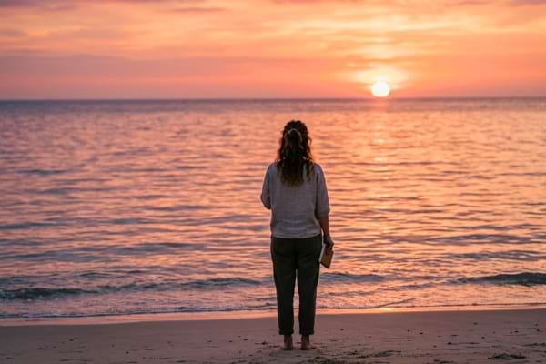Une femme pensive et sereine de dos qui regarde un magnifique coucher de soleil