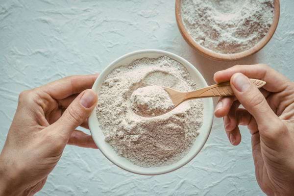 une cuillere prend de la farine dans un bol tenu par des mains