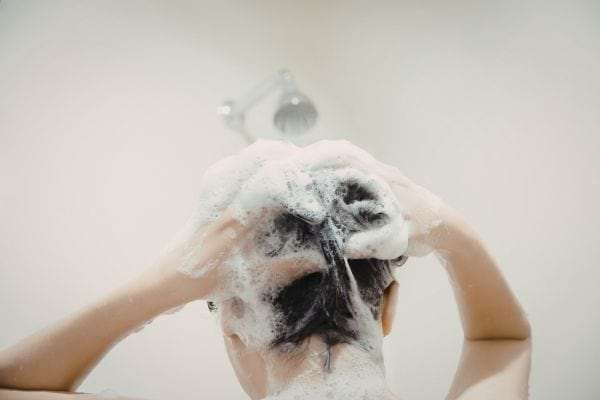 une personne lave ses cheveux sous la douche avec beaucoup de mousse