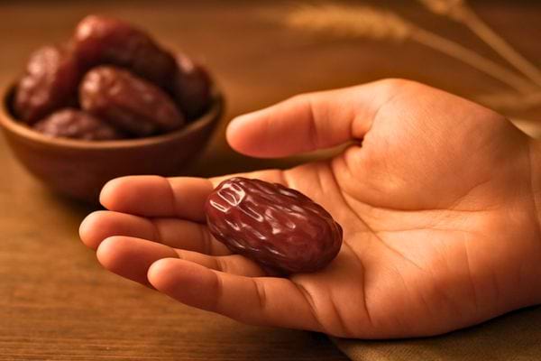 une main tient une datte brune tandis quun bol de dattes est pose en arriere plan