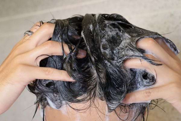 des mains massent les cheveux mouilles avec du shampoing mousseux