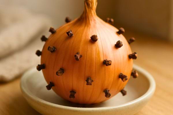 un oignon rempli de clous de girofle pose dans une petite assiette