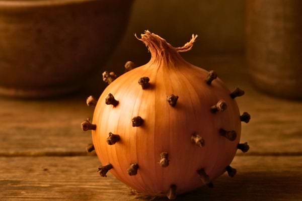 un oignon pique de plusieurs clous de girofle pose sur une table en bois
