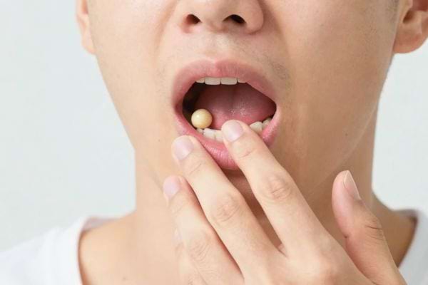 une personne met un petit comprime dans sa bouche avec ses doigts