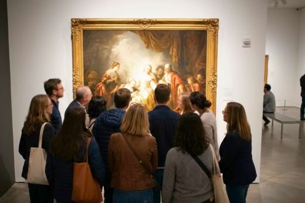 A crowd of modern museum visitors looking at a large framed painting on a gallery wall.