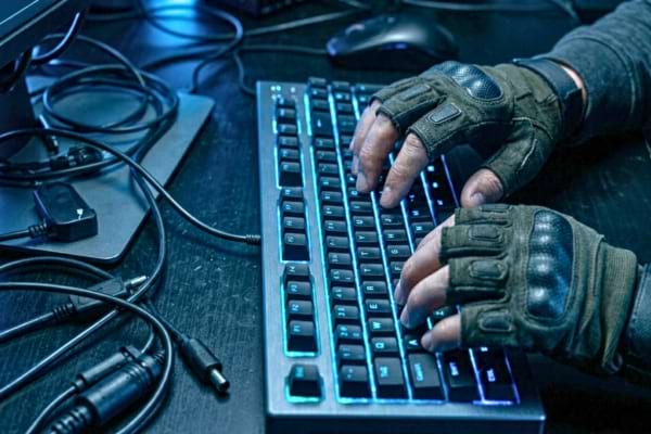 mains d'un hacker encapuchonn&eacute; tapant sur un clavier r&eacute;tro&eacute;clair&eacute; dans la p&eacute;nombre