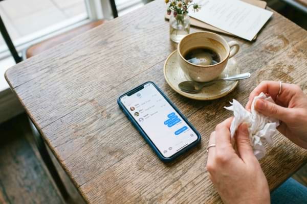 un smartphone posé sur une table de café en bois. L'écran affiche des messages laissés "en attente" ou "lus