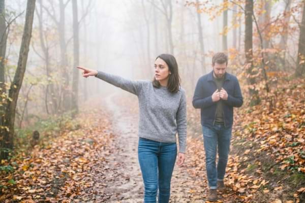 Une femme regarde vers l'avant en pointant du doigt une direction, tandis que l'homme regarde ses pieds,
