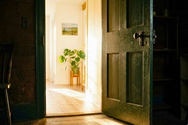 une porte entrouverte laissant entrer une lumi&egrave;re vive et chaleureuse dans une pi&egrave;ce sombre