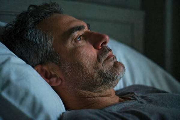 un homme de 50 ans aux tempes grisonnantes, allong&eacute; sur un oreiller blanc, les yeux ouverts