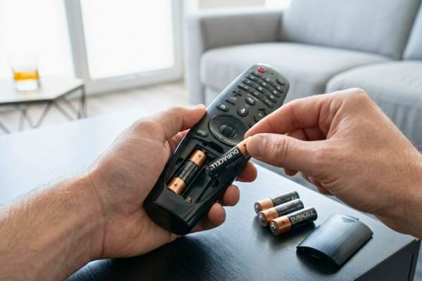 une personne retirant les piles AA d'une t&eacute;l&eacute;commande noire