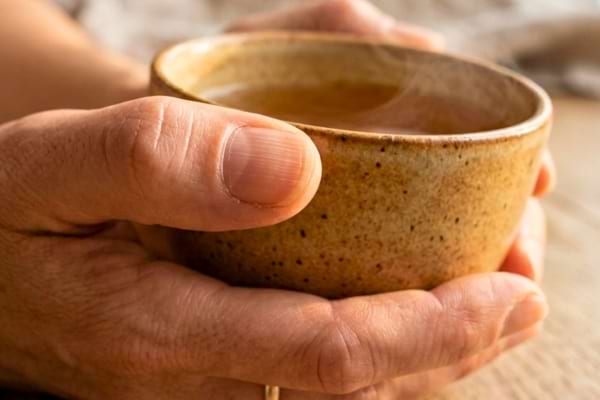 doigts d'une personne d'&acirc;ge m&ucirc;r tenant une tasse de th&eacute; fumante en c&eacute;ramique.