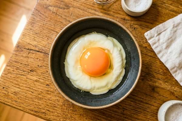 une belle assiette en c&eacute;ramique mate. Un &oelig;uf cru fra&icirc;chement cass&eacute; y repose.