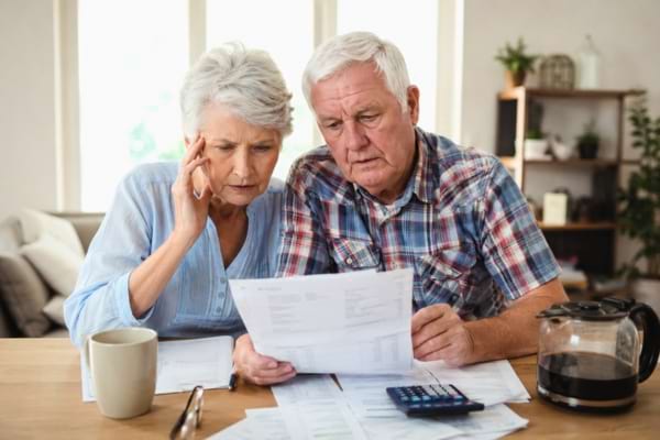 un couple de seniors soucieux, assis &agrave; la table de leur salon, regardant attentivement des factures