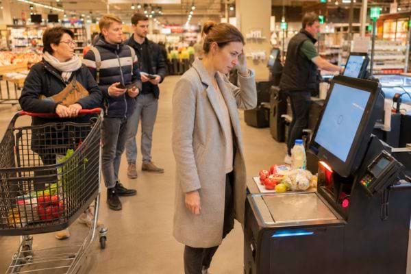 Cliente perplexe devant une caisse automatique au supermarch&eacute;.