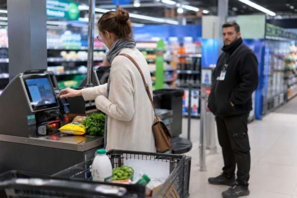 Femme utilisant une caisse automatique sous le regard d&rsquo;un employ&eacute;.