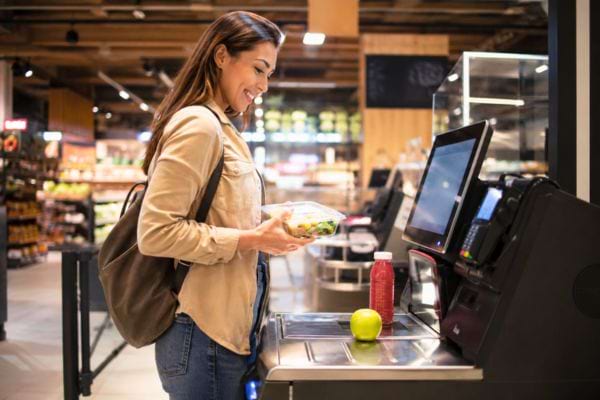 Cliente souriante scannant ses courses &agrave; une caisse automatique.