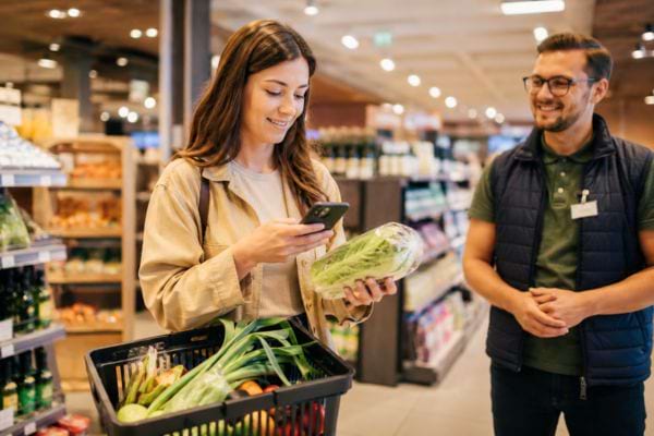 Femme v&eacute;rifiant un article sur son t&eacute;l&eacute;phone avec un employ&eacute;.