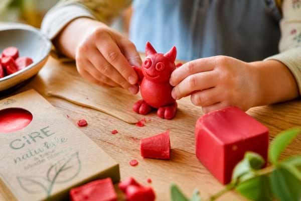 mains modelant une petite figurine amusante avec de la cire rouge souple,