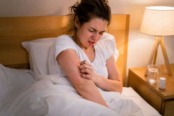 Femme dans son lit se grattant le bras avec une &eacute;ruption cutan&eacute;e