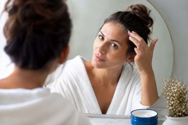Femme lissant ses petits frisottis avec une noisette de cr&egrave;me devant un miroir.
