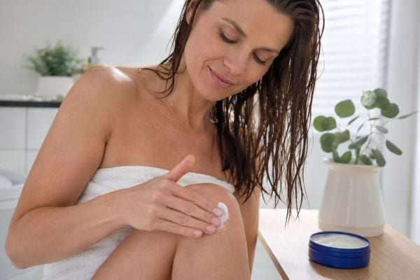 Femme appliquant une cr&egrave;me hydratante sur son genou apr&egrave;s la douche.