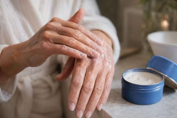Femme appliquant une cr&egrave;me hydratante sur ses mains s&egrave;ches.