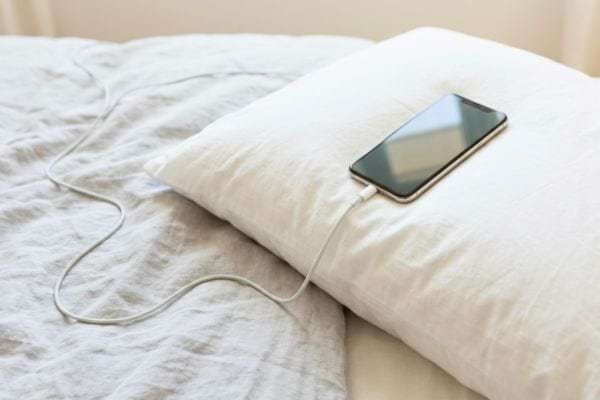 Smartphone en charge pos&eacute; sur un oreiller sur un lit
