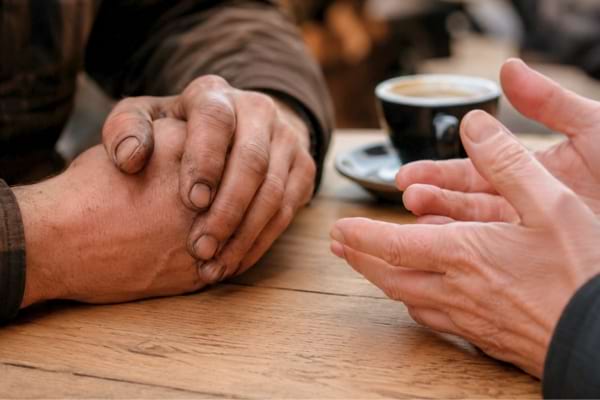 deux mains posées sur une table de café en bois clair. L'une des mains présente des ongles visiblement noircis par la terre.