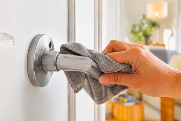 Main nettoyant une poign&eacute;e de porte avec un chiffon gris.