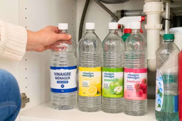 Bouteilles de vinaigre ménager rangées sous un évier.