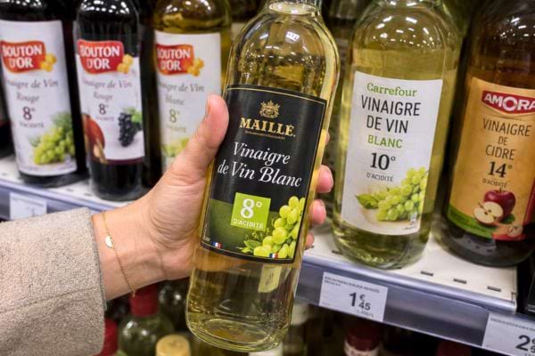 Main tenant une bouteille de vinaigre de vin blanc en rayon.